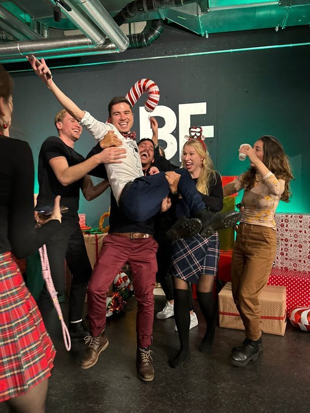 Friends lifting a laughing dancer in the air at a Christmas party at The Vibe Dance Studio in Zurich.